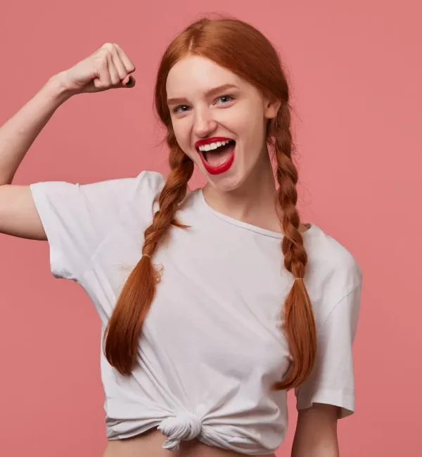 indoor-portrait-young-ginger-female-with-freckles-posing-pink-background-showing-her-biceps-smiles-broadly-scaled-1-1